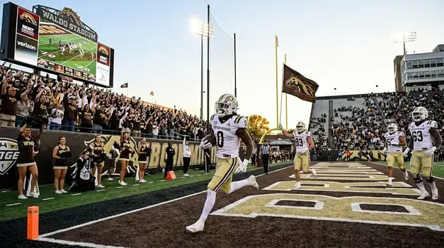 Western Michigan Broncos football player running into the end zone for a touchdown at Waldo Stadium in front of cheering fans.